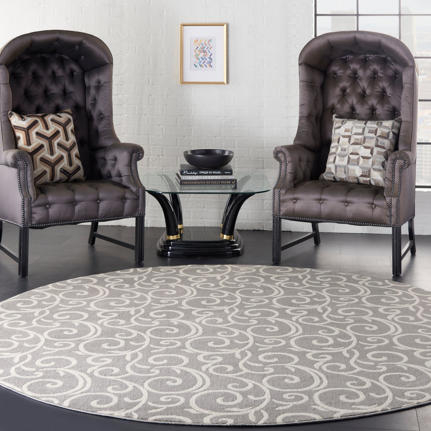 Round grey swirl-pattern rug (8' round) on the floor, flanked by two dark brown tufted leather armchairs with nailhead trim and a glass round coffee table.