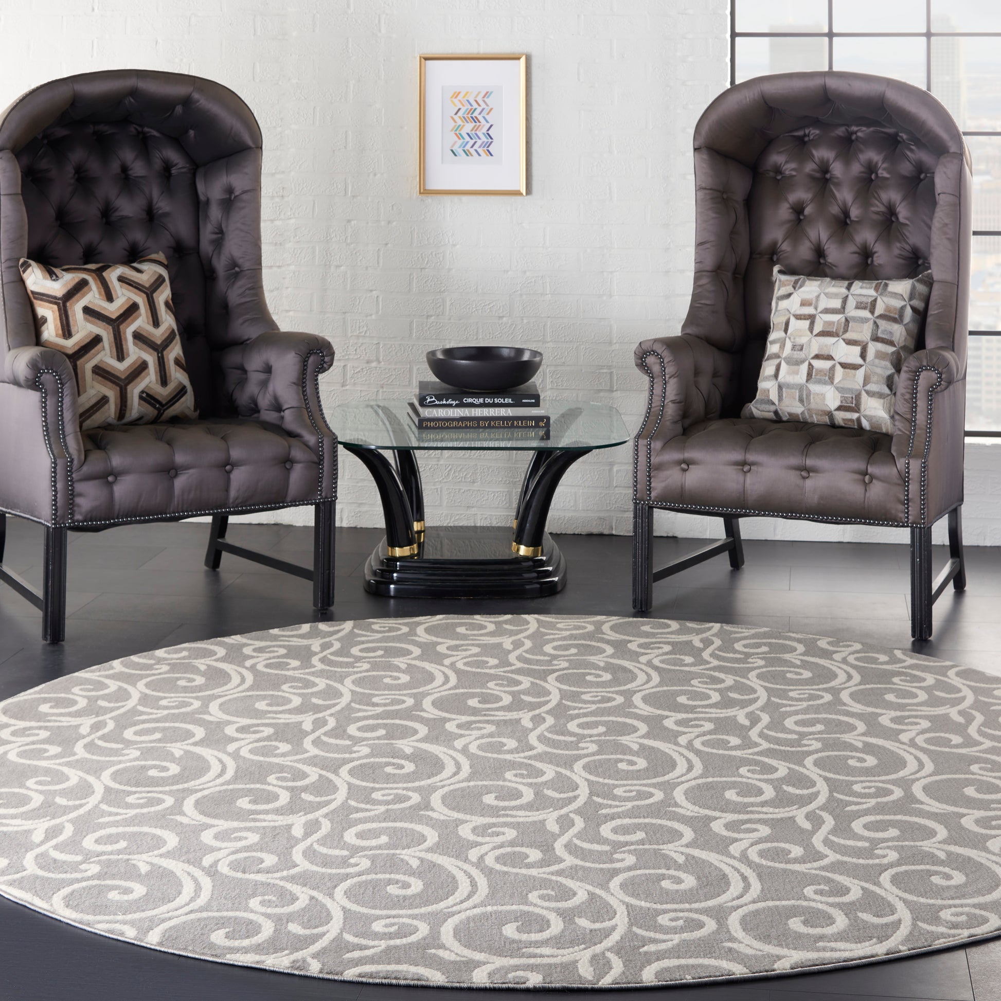 Round grey swirl-pattern rug (8' round) on the floor, flanked by two dark brown tufted leather armchairs with nailhead trim and a glass round coffee table.