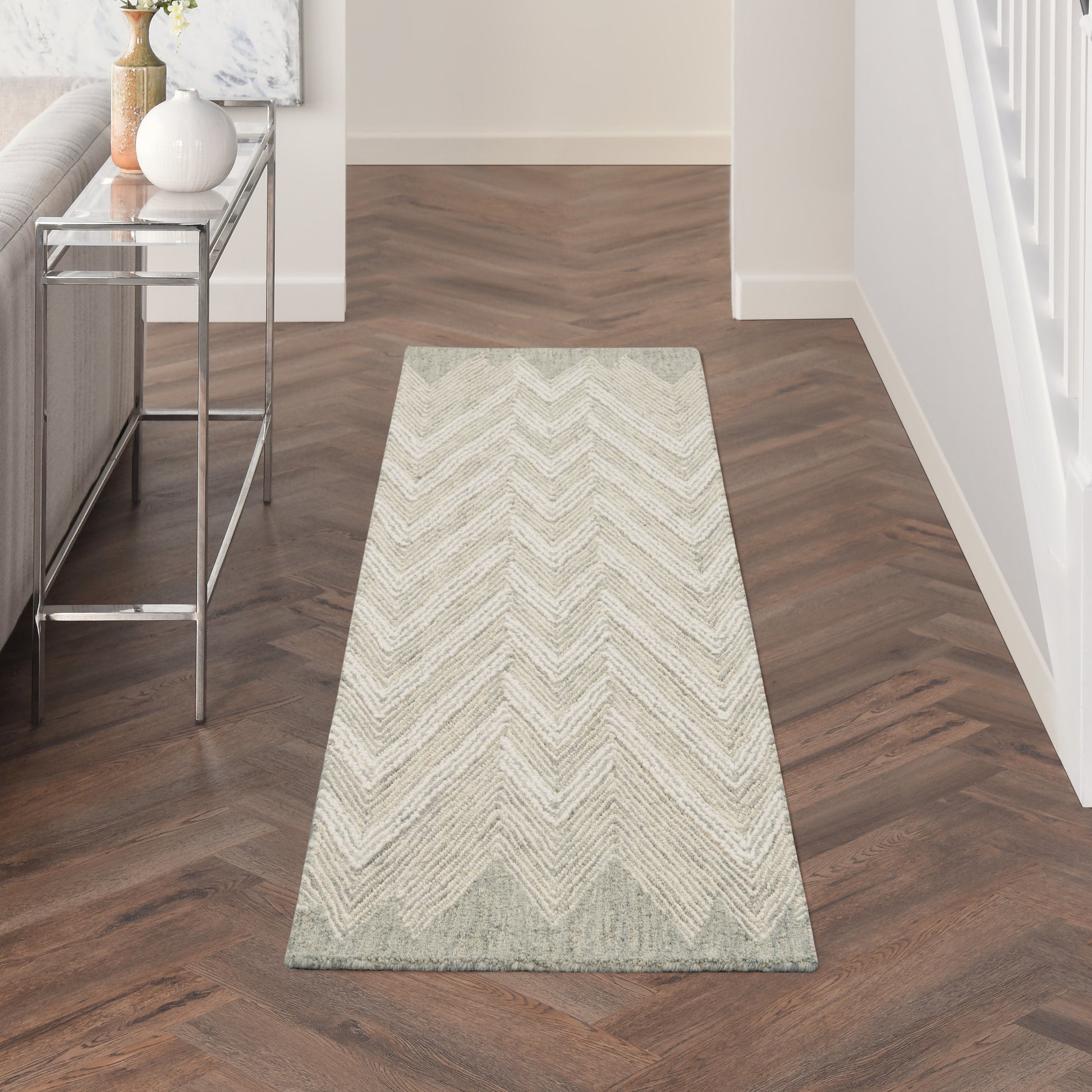 Long light beige chevron rug runner on dark wood herringbone floor; modern entryway with chrome console on left.