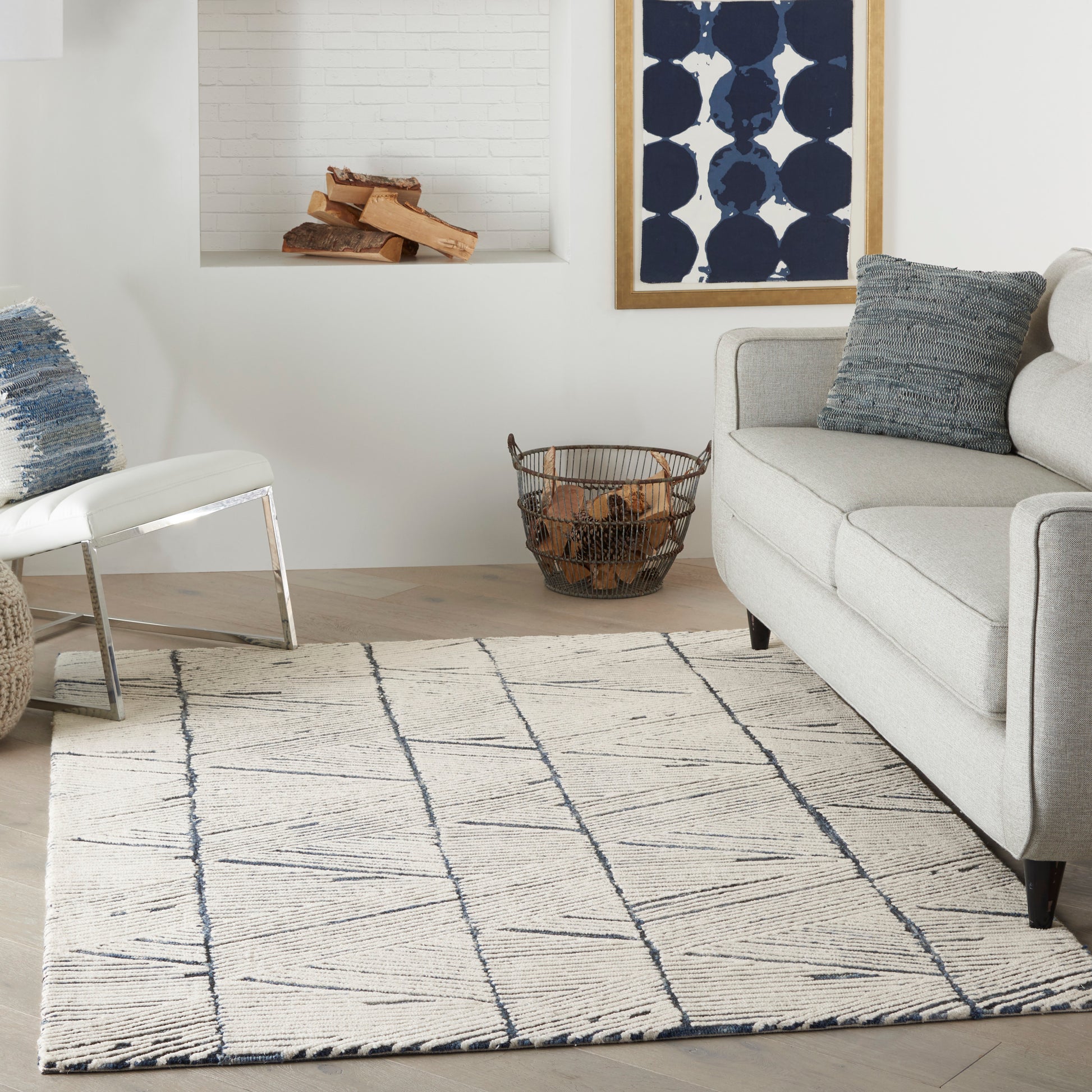 Beige rug with navy geometric lines in a modern living room with gray sofa, blue pillows, white chair, and navy framed art.