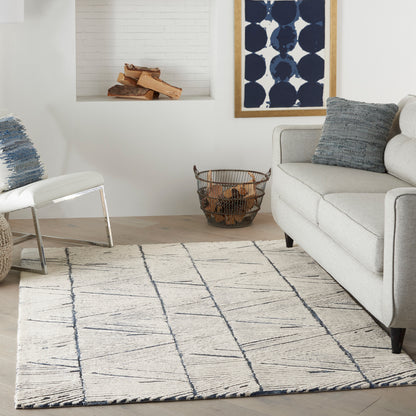Beige rug with navy geometric lines in a modern living room with gray sofa, blue pillows, white chair, and navy framed art.