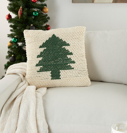 Cream chunky-knit square pillow with dark green Christmas tree motif on a beige sofa, paired with a cozy knit throw.