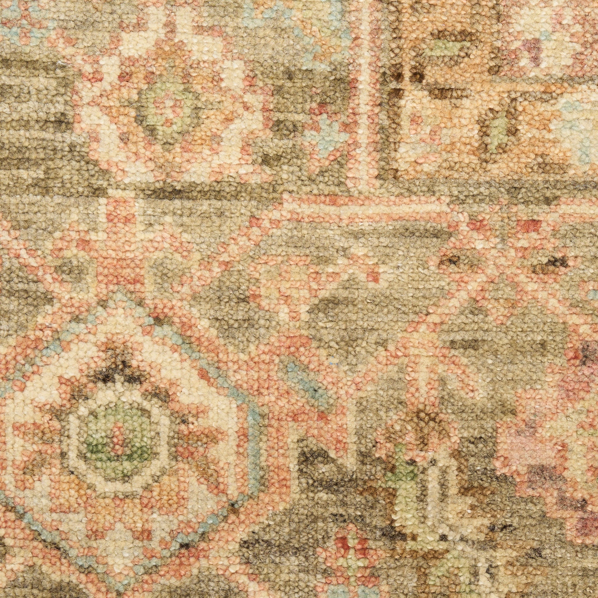 Close-up of a textured oriental rug with beige, pink, and sage green geometric motifs.