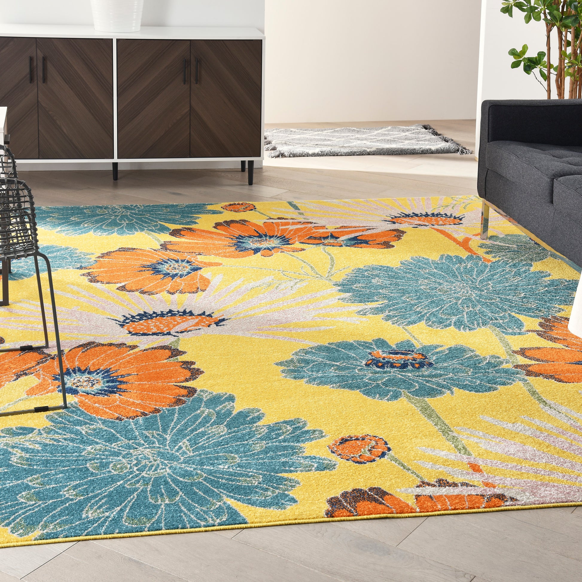 Bright yellow floral area rug with oversized teal and orange petals, woven texture in a modern living room.