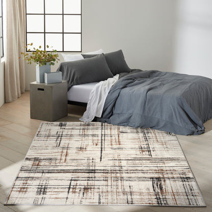 Dark gray duvet and pillows with white sheets on a bed, cream-brown abstract rug, and a concrete nightstand with plant.