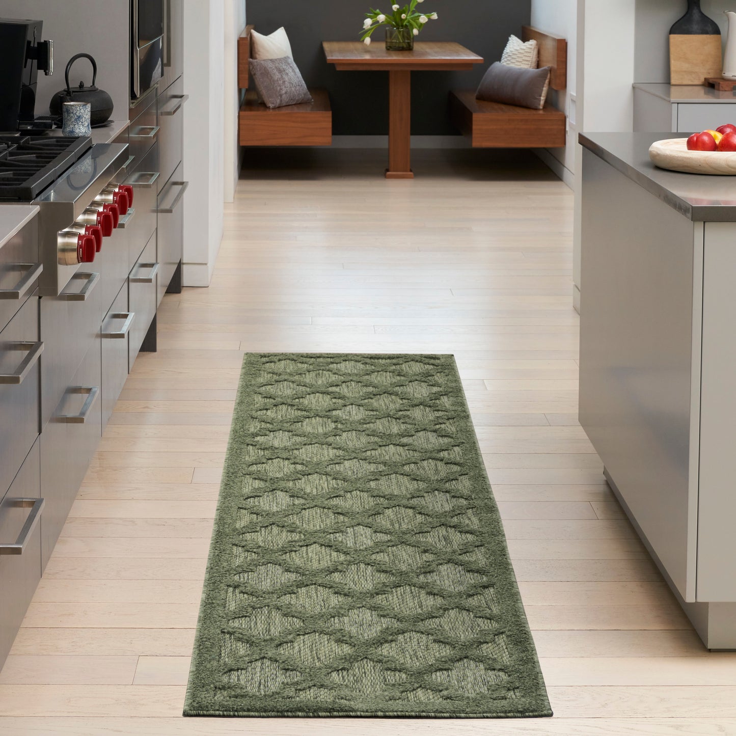 Green diamond-pattern runner rug on light hardwood kitchen floor in a modern kitchen with stainless appliances.