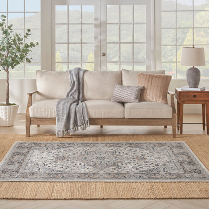 Beige linen sofa with gray throw and textured pillows, wooden legs; blue-gray oriental rug over natural jute.