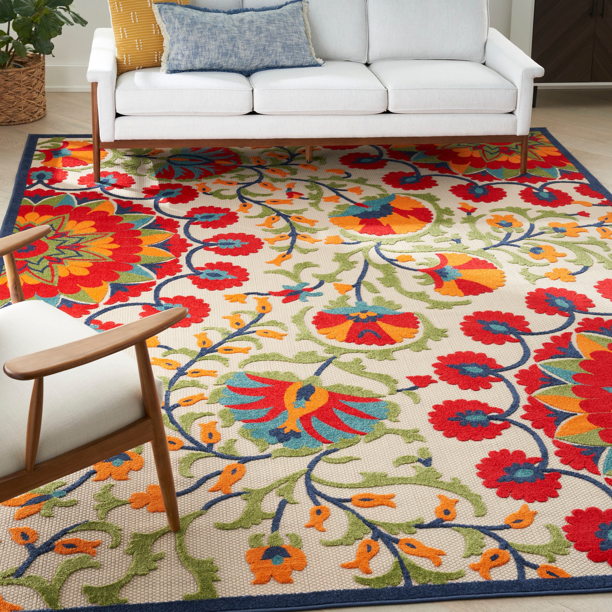 Colorful floral area rug with red, orange, blue flowers on a cream background; paired with a white sofa and wooden chair.