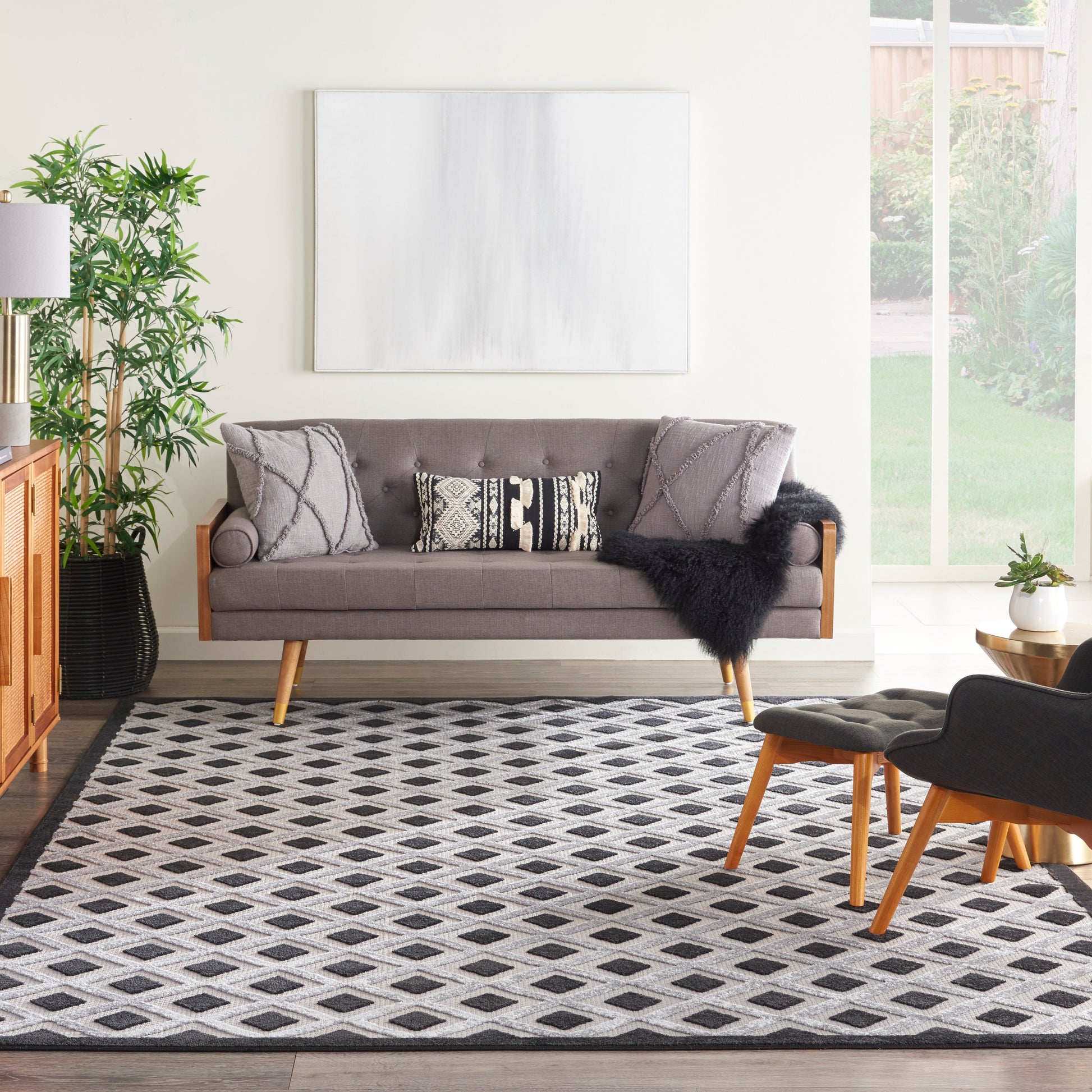 Cozy living room with gray mid-century sofa, wooden legs, geometric cushions, black faux-fur throw, and a diamond rug.