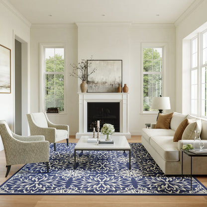 Bright living room with white walls, beige sofa, two patterned armchairs, a blue floral rug, and a fireplace.
