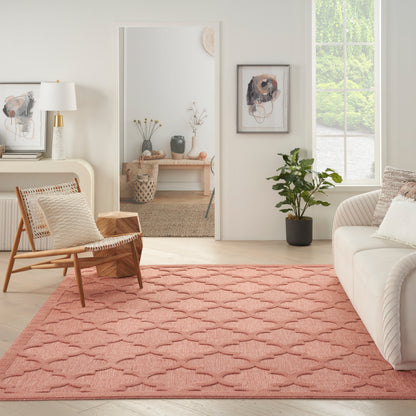 Pink scallop-patterned area rug brightens a living room with beige sofa, wooden woven chair, mirror, and potted plant.