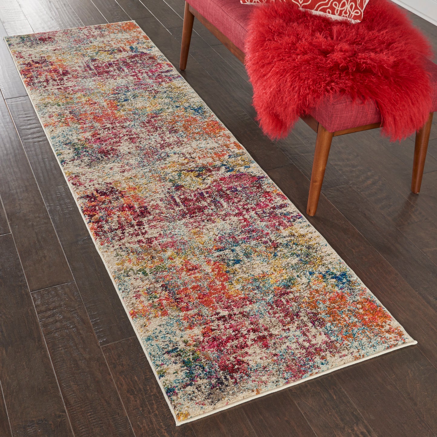 Long rectangular multicolor shag runner rug on dark wood floor beside a pink upholstered chair with a red fluffy faux-fur throw.