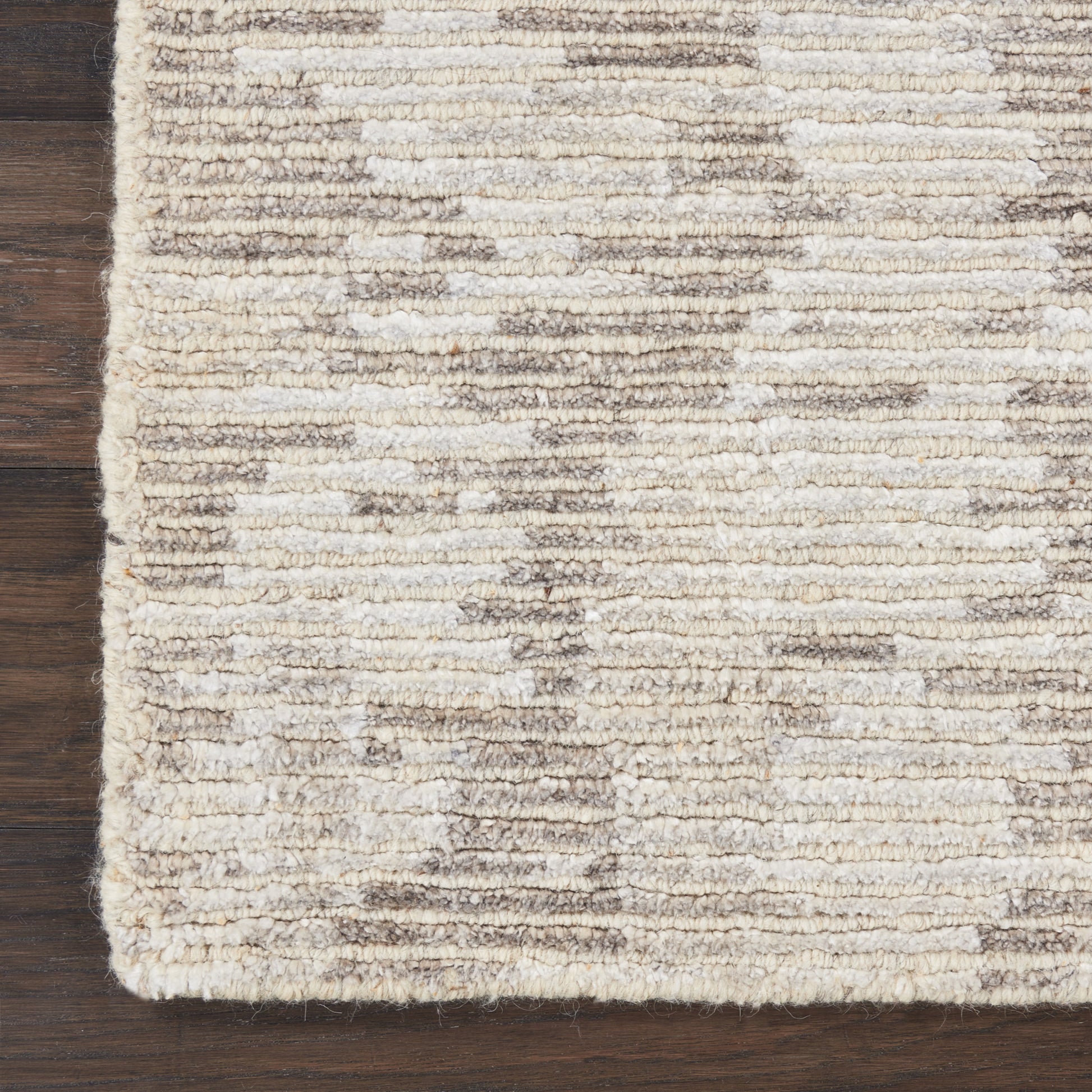 Beige textured rug with cream and taupe horizontal stripes on dark wood floor.