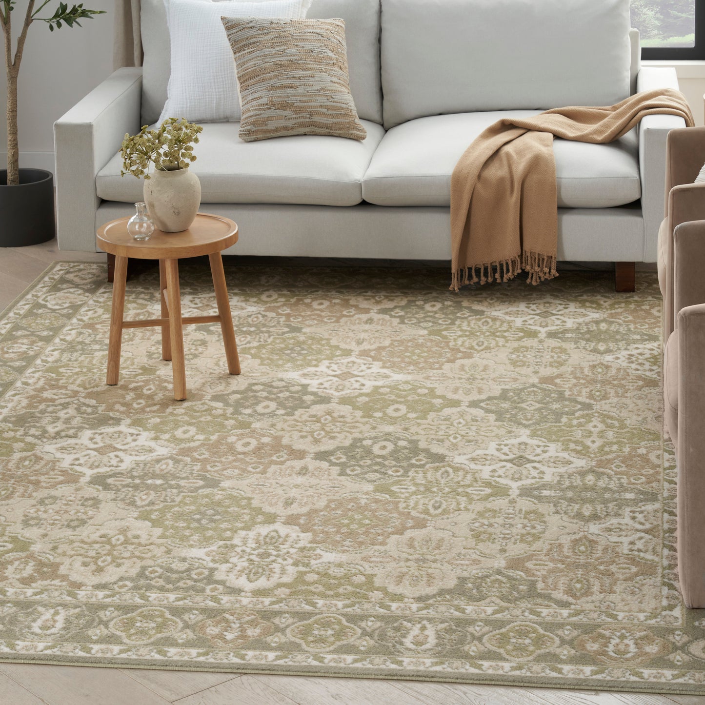 Beige area rug with cream floral medallion pattern in a cozy living room with a light gray sofa and wooden side table.