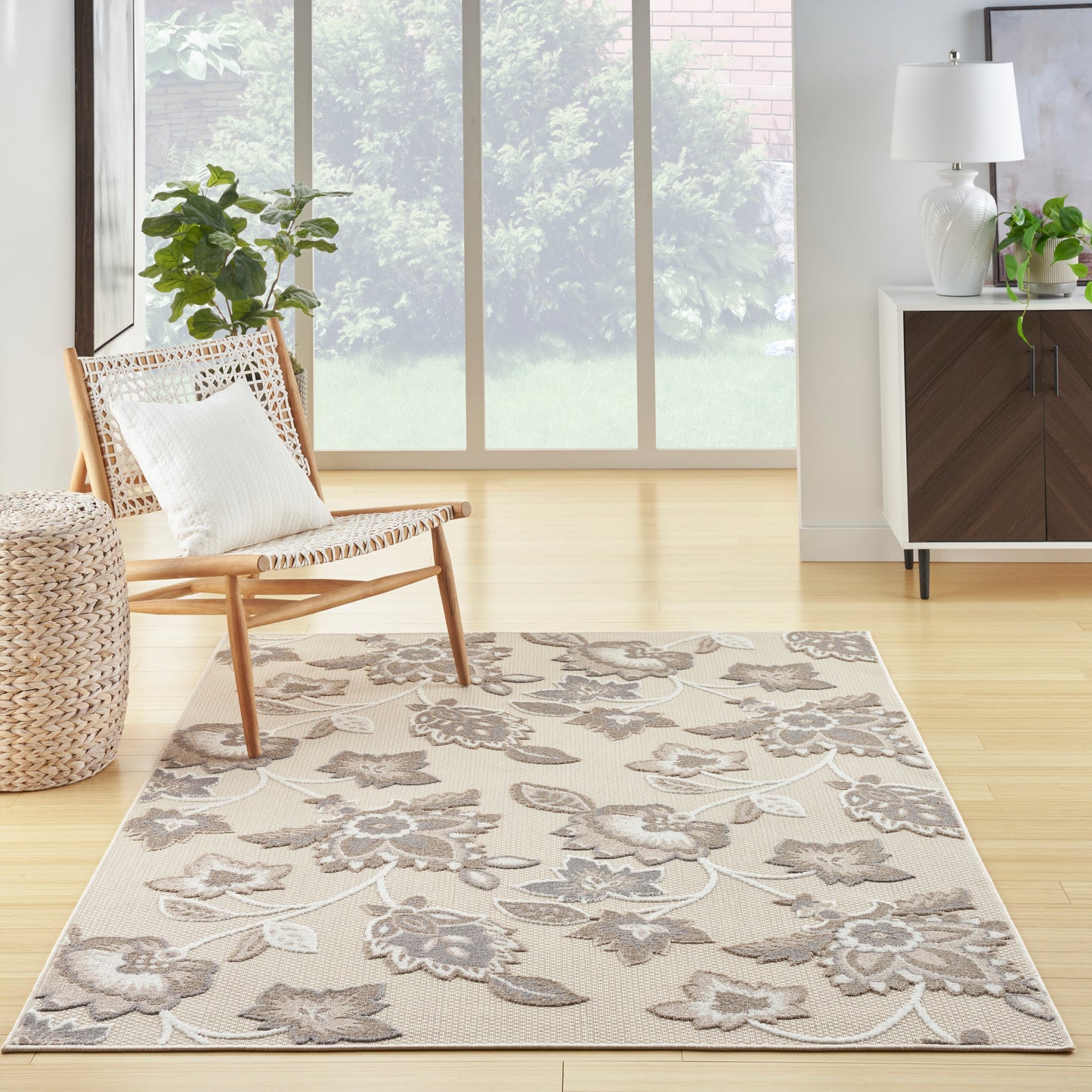 Beige floral area rug with gray vines in a bright living room; light wood floor, wicker chair, and modern cabinet.