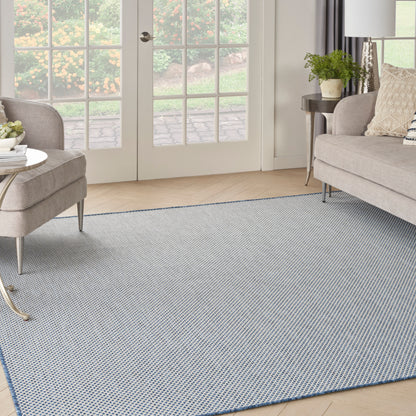 Soft blue-gray woven area rug in a beige living room with two light sofas, glass doors, and a small side table with plant.