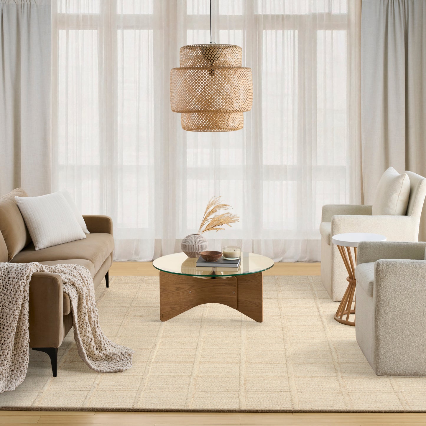 Neutral living room with beige sofa, knit throw, round glass coffee table, woven pendant light, armchairs, sheer curtains.