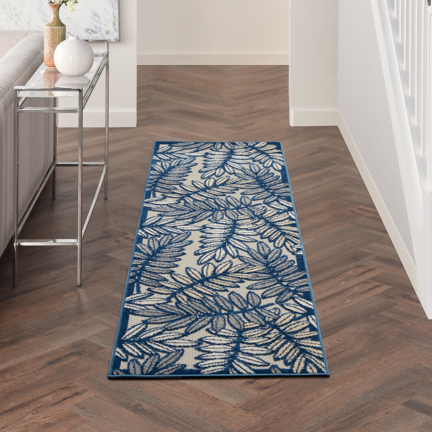 Leaf-patterned blue hallway runner rug with cream background and teal border on wood floor.