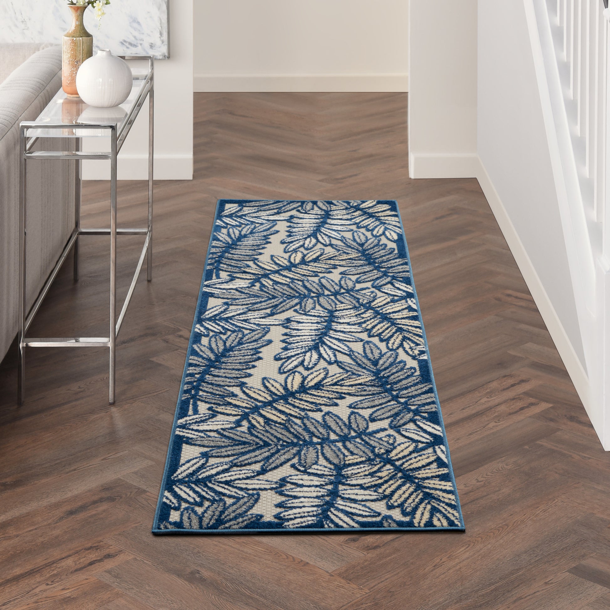 Leaf-patterned blue hallway runner rug with cream background and teal border on wood floor.