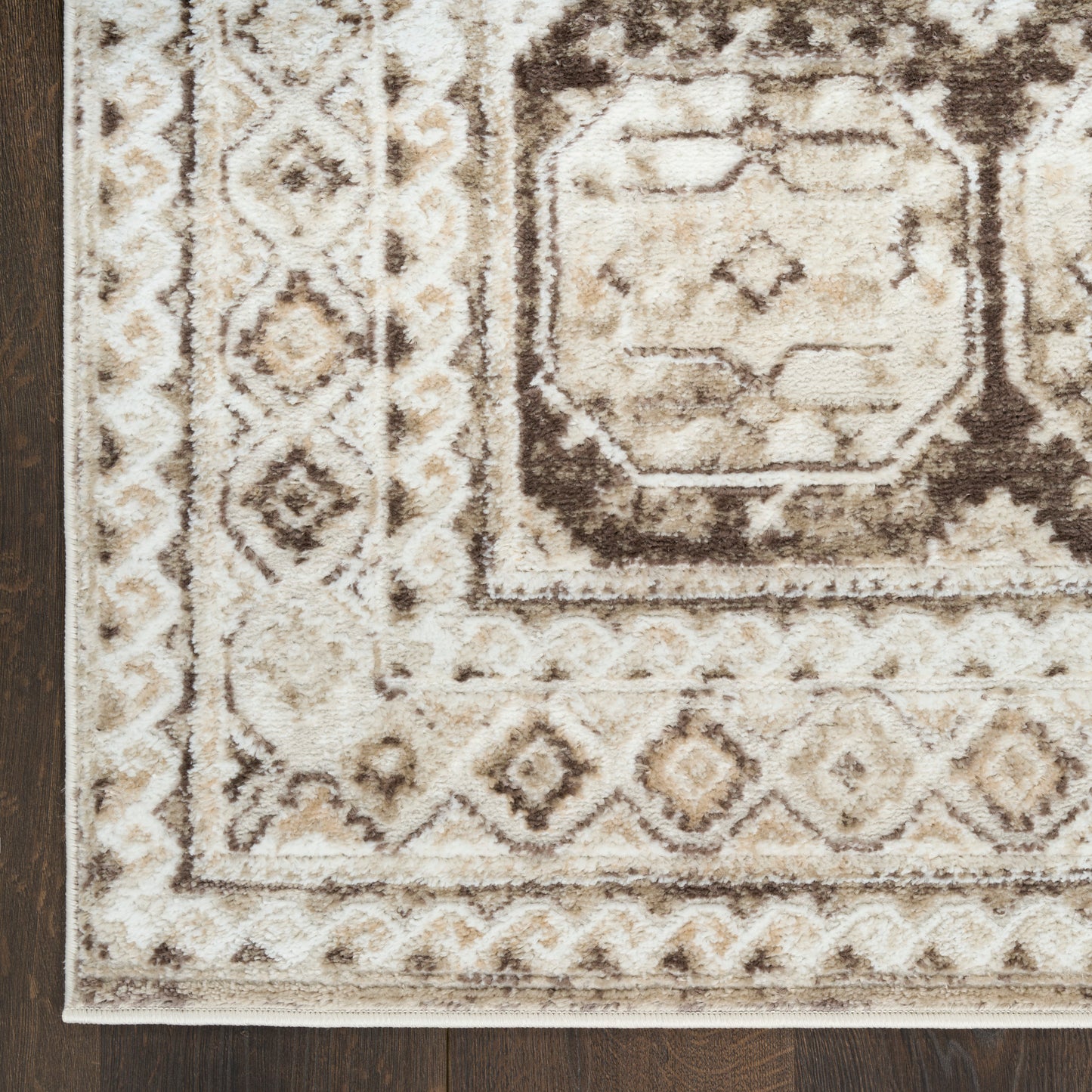 Ivory, beige & brown oriental area rug with geometric medallion & border pattern on dark wood floor.