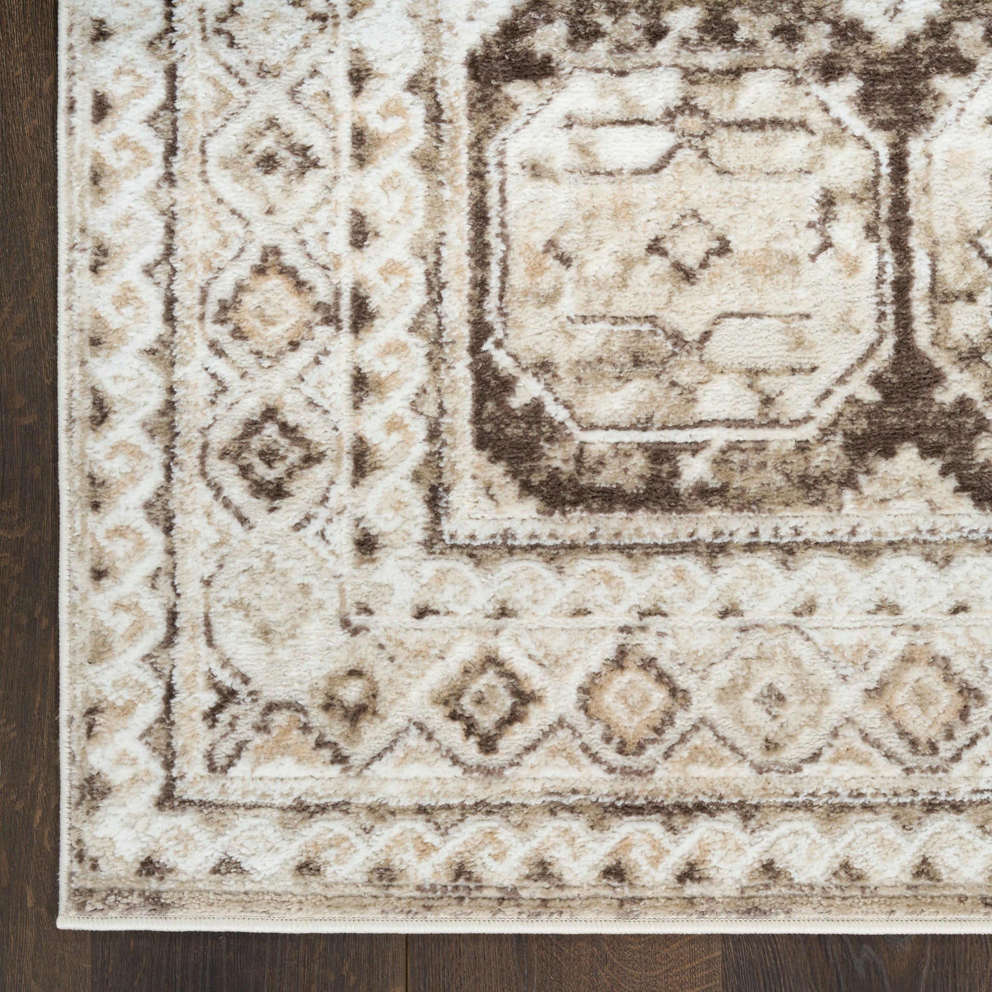 Ivory, beige & brown oriental area rug with geometric medallion & border pattern on dark wood floor.
