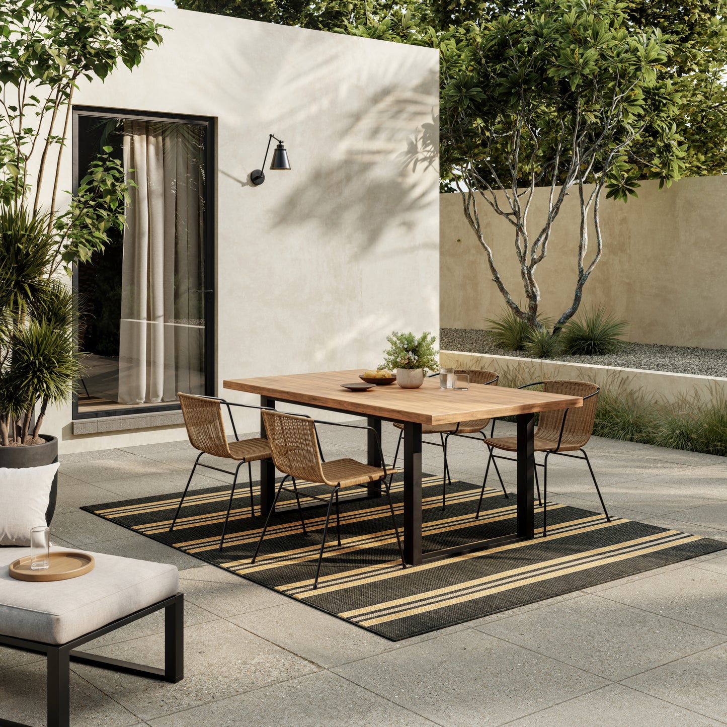 Outdoor dining set: rectangular wooden table with black metal legs and six wicker chairs on striped outdoor rug amid garden.