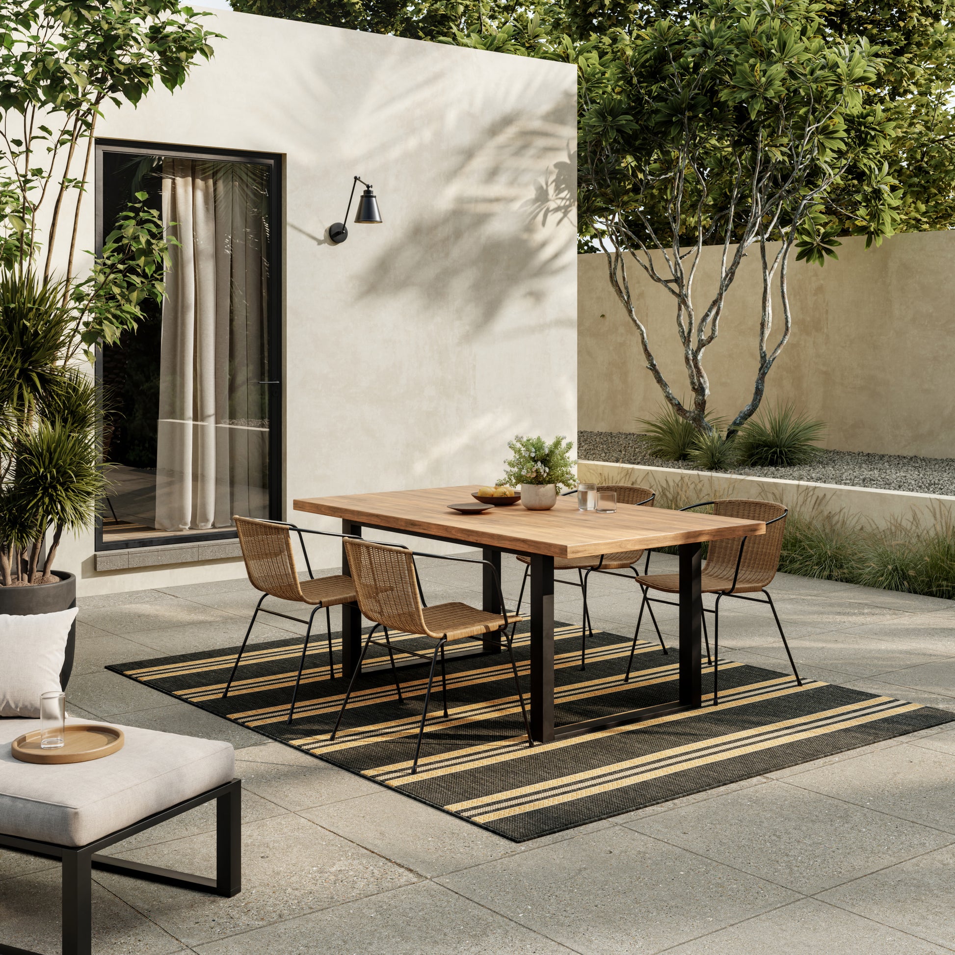 Outdoor dining set: rectangular wooden table with black metal legs and six wicker chairs on striped outdoor rug amid garden.