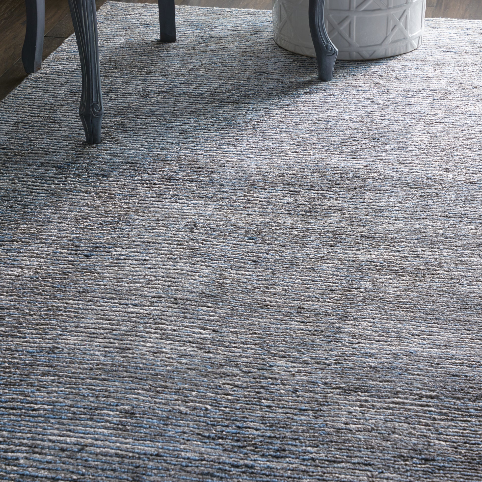 Blue-gray textured area rug with subtle linear pattern, paired with dark metal chair legs and a white geometric planter.