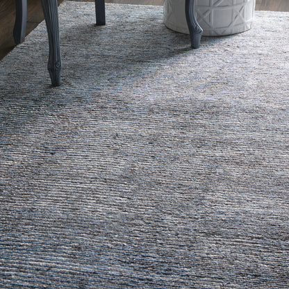 Blue-gray textured area rug with subtle linear pattern, paired with dark metal chair legs and a white geometric planter.