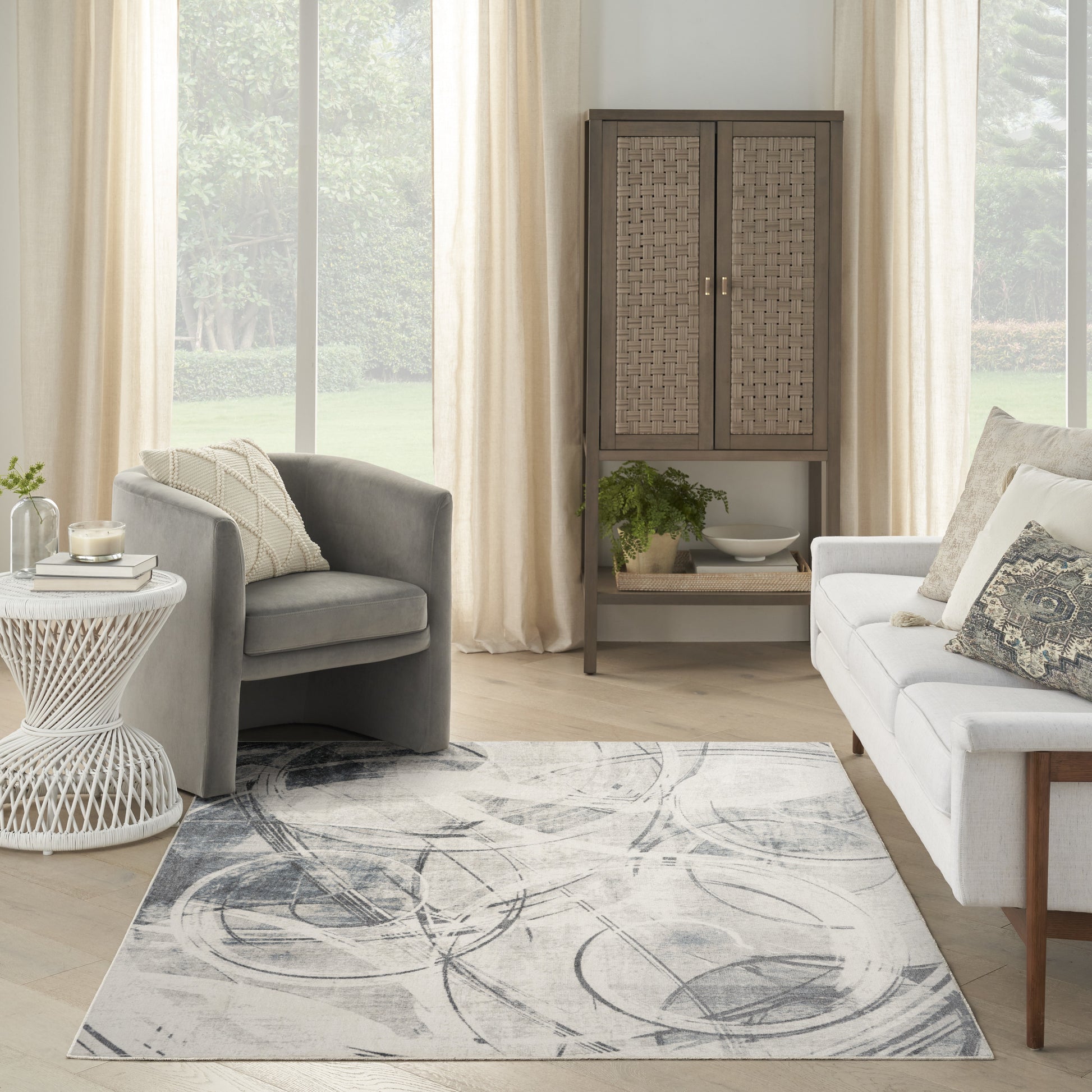 Neutral living room with gray fabric chairs, white sofa, beige curtains, a woven-rattan cabinet, and an abstract gray rug.