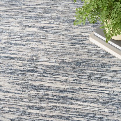 Blue abstract striped area rug with textured weave; corner features a green potted plant and stacked books.