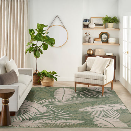 Green tropical leaf area rug anchors a light living room with beige sofa, striped armchair, shelves and potted plants.