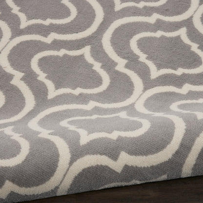 Gray round rug with white quatrefoil trellis pattern on dark wood floor