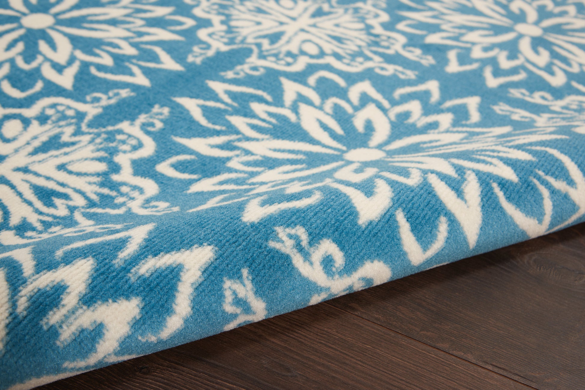 Blue and white floral-patterned rug with bold blossoms, woven textile on dark wood floor.