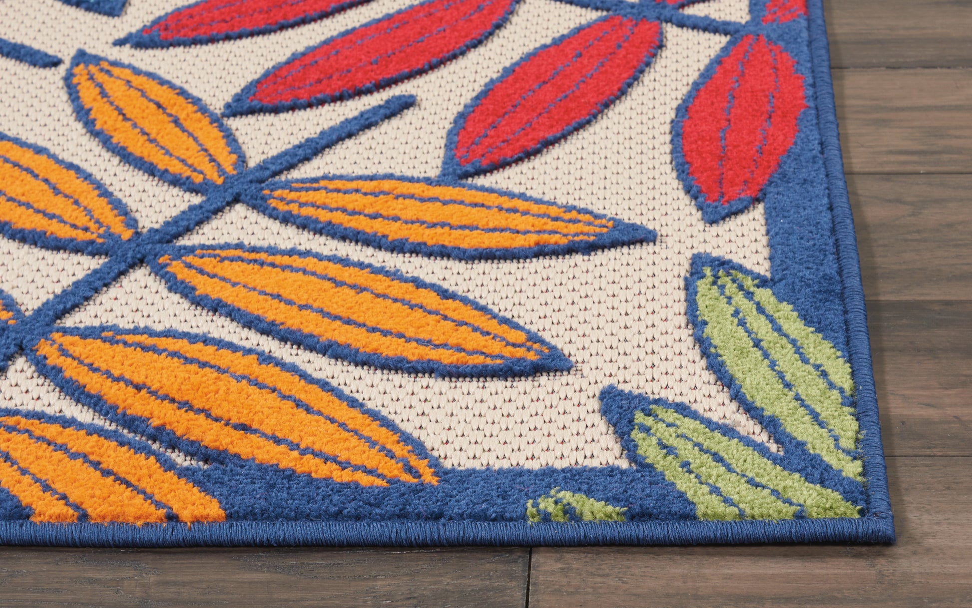 Vibrant leaf-print rug with orange, yellow, red and green leaves on cream field and blue border on wood floor.