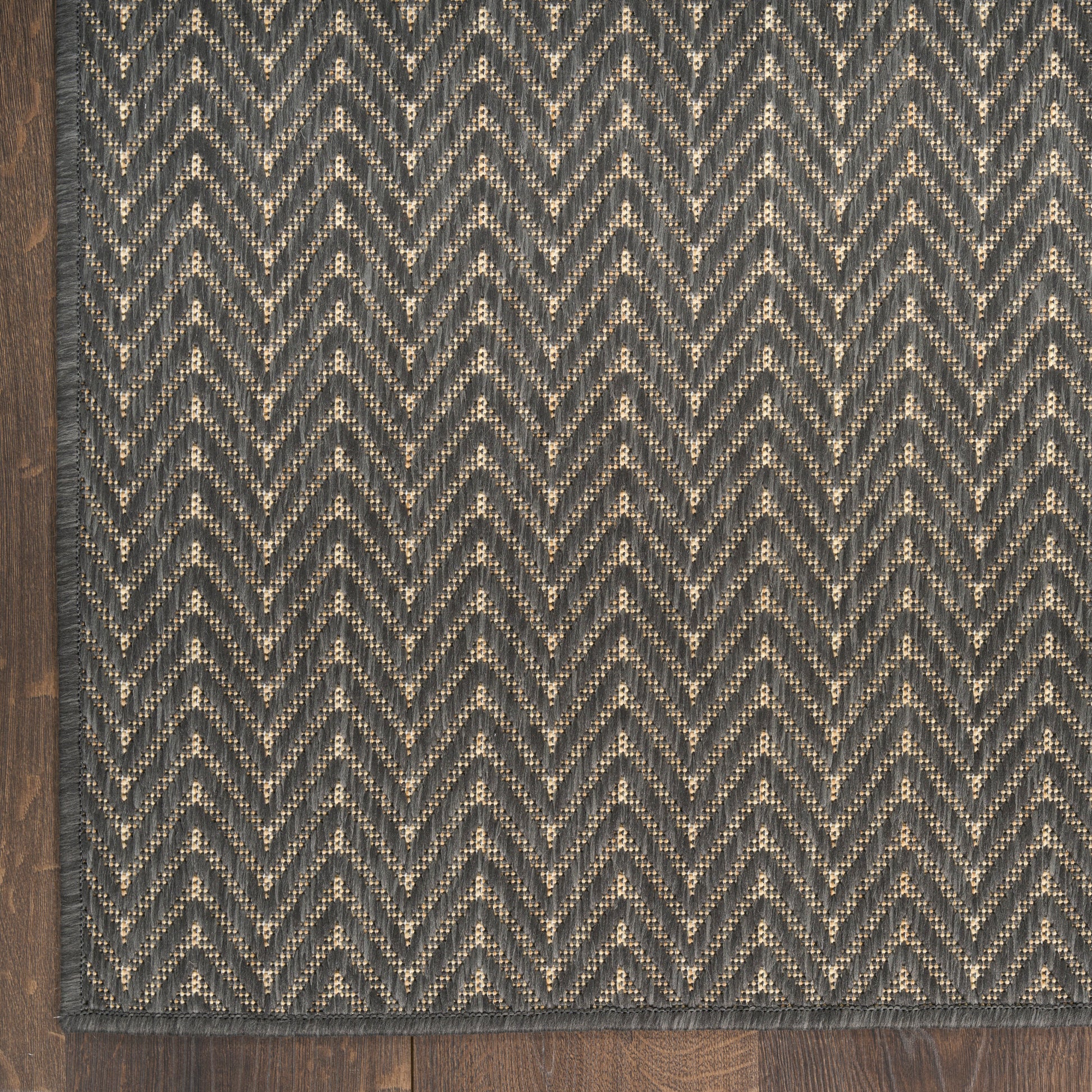 Rectangular charcoal rug with beige chevron pattern and woven texture on dark wood floor.