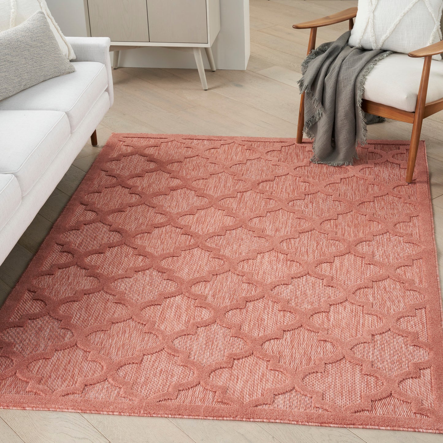 Coral-pink flatweave area rug with a repeating trellis/quatrefoil pattern, in a modern living room.