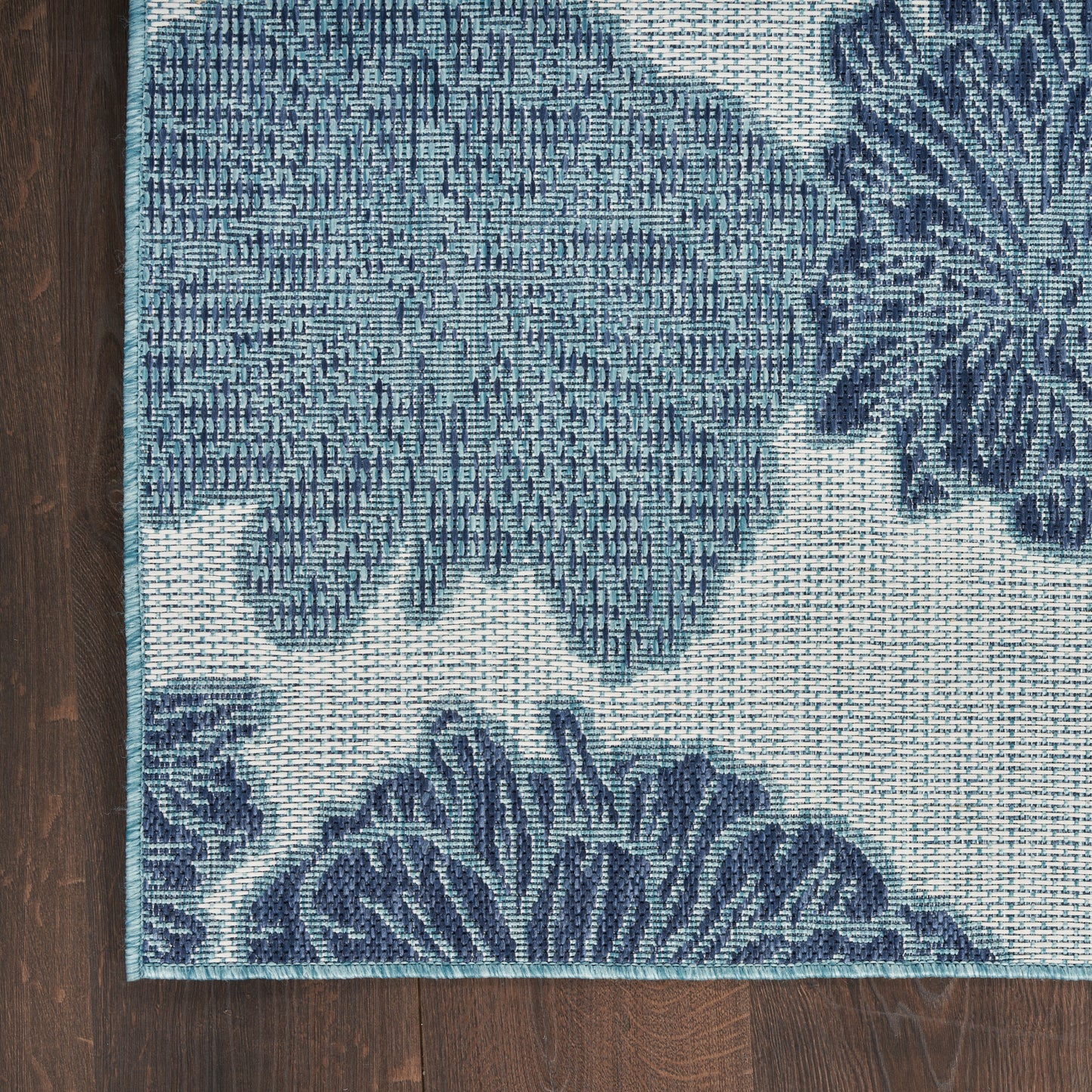 Rectangular blue floral woven area rug with teal border on dark wood floor.