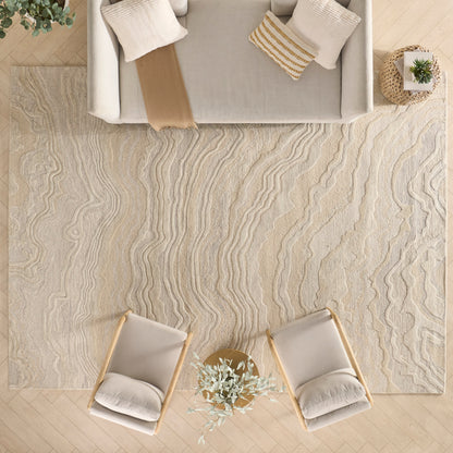 Top-down view: beige wavy rug, two cream armchairs around a small round table with a plant, beige sofa with cushions.