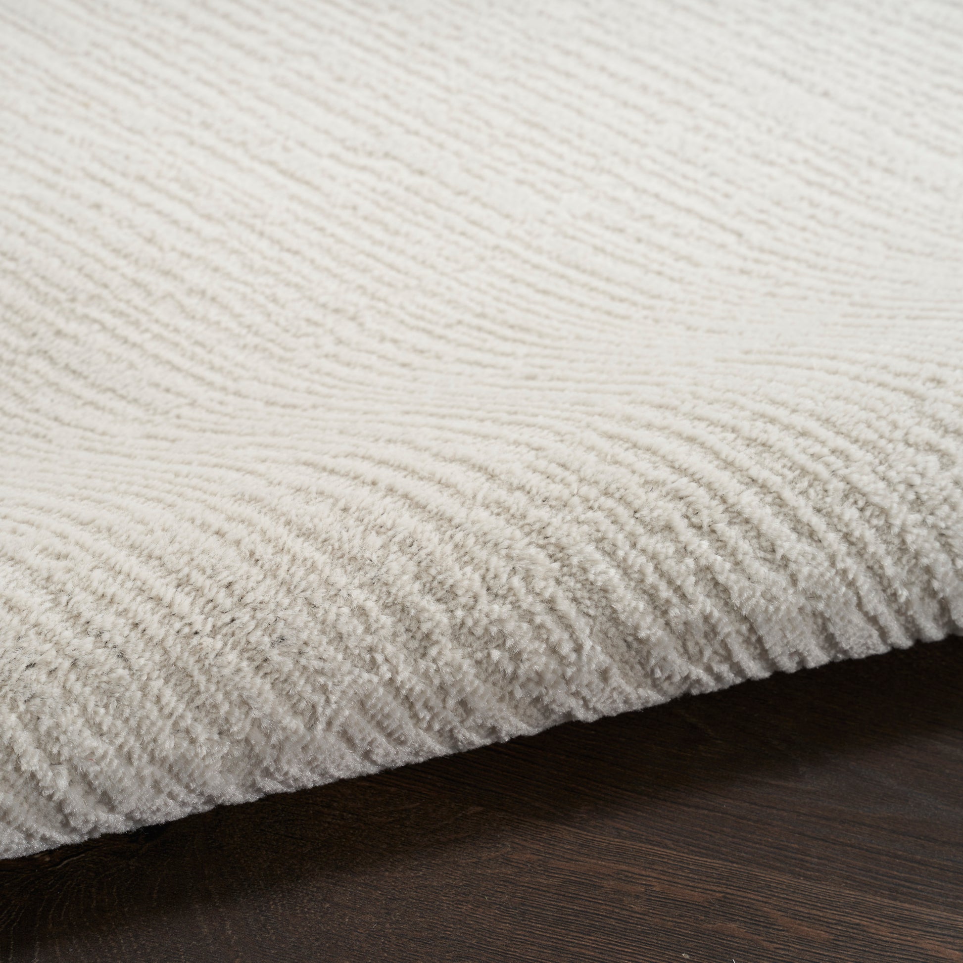 Cream textured rug with soft, ribbed pile on dark wood floor.