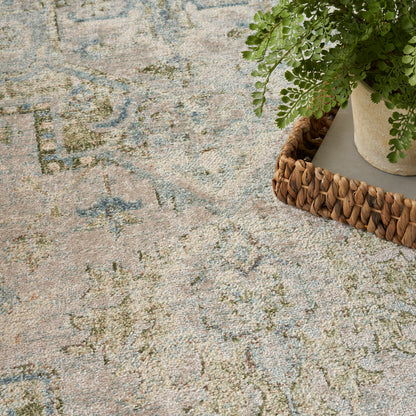 Beige vintage rug with blue-green scroll pattern; woven straw basket and potted fern resting on edge.