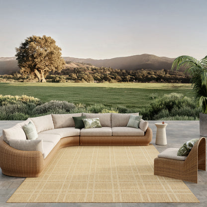 Outdoor tan rug with beige cushions and green pillows; scenic countryside backdrop.
