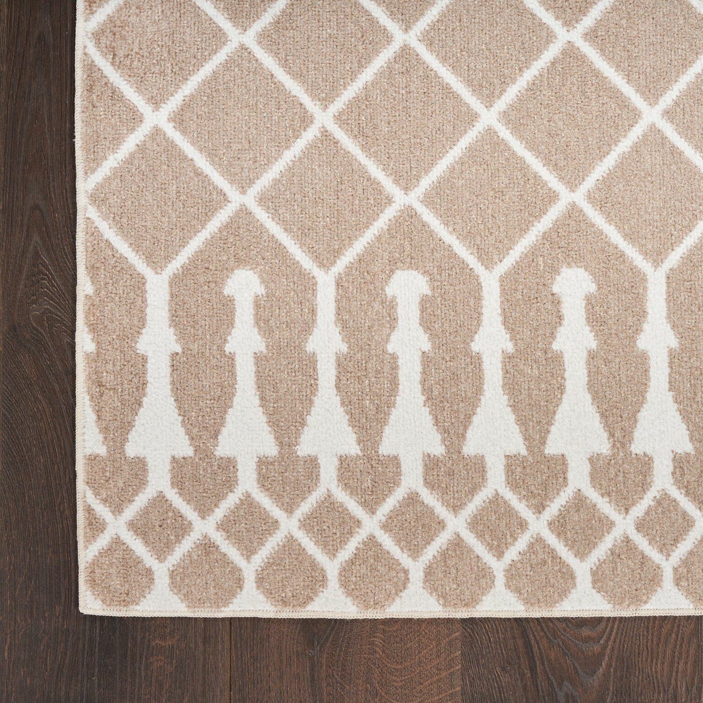 Beige woven runner rug with white lattice diamonds and arched border motifs on dark wood floor.
