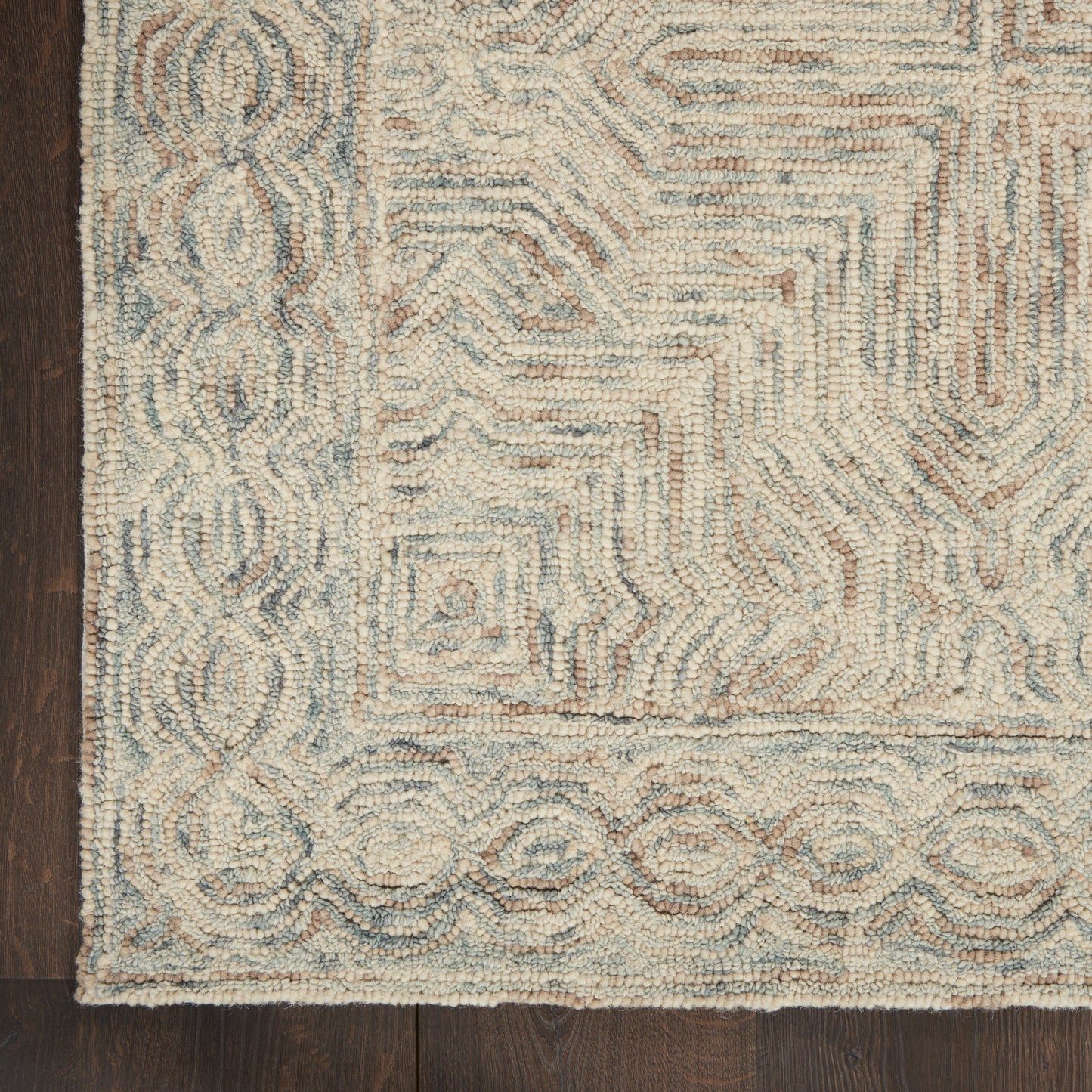 Beige tufted area rug with blue-gray geometric maze center and decorative circular border on dark wooden floor.