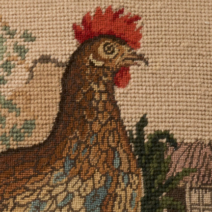 Needlepoint tapestry close-up of a brown hen with red comb, blue and tan feather pattern, green foliage in background.