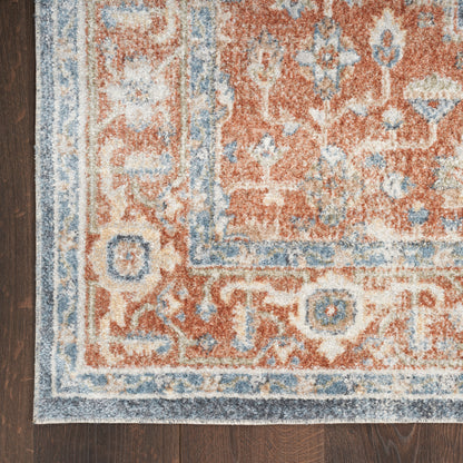 Close-up of a woven wool rug with red, blue and cream tones and a floral border on a dark wood floor.