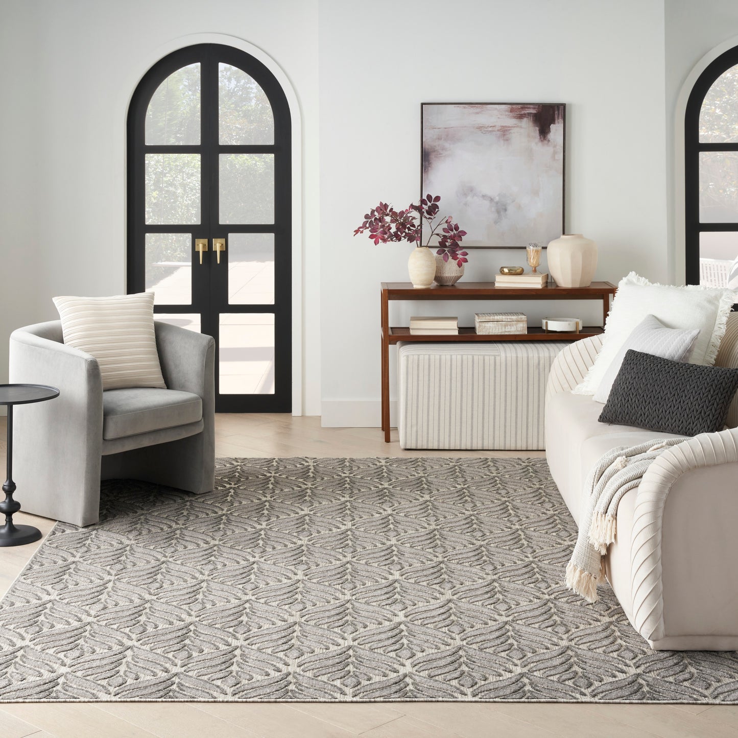 Neutral living room: arched black doors, gray armchair, beige sofa, wooden console, and geometric leaf-patterned gray rug