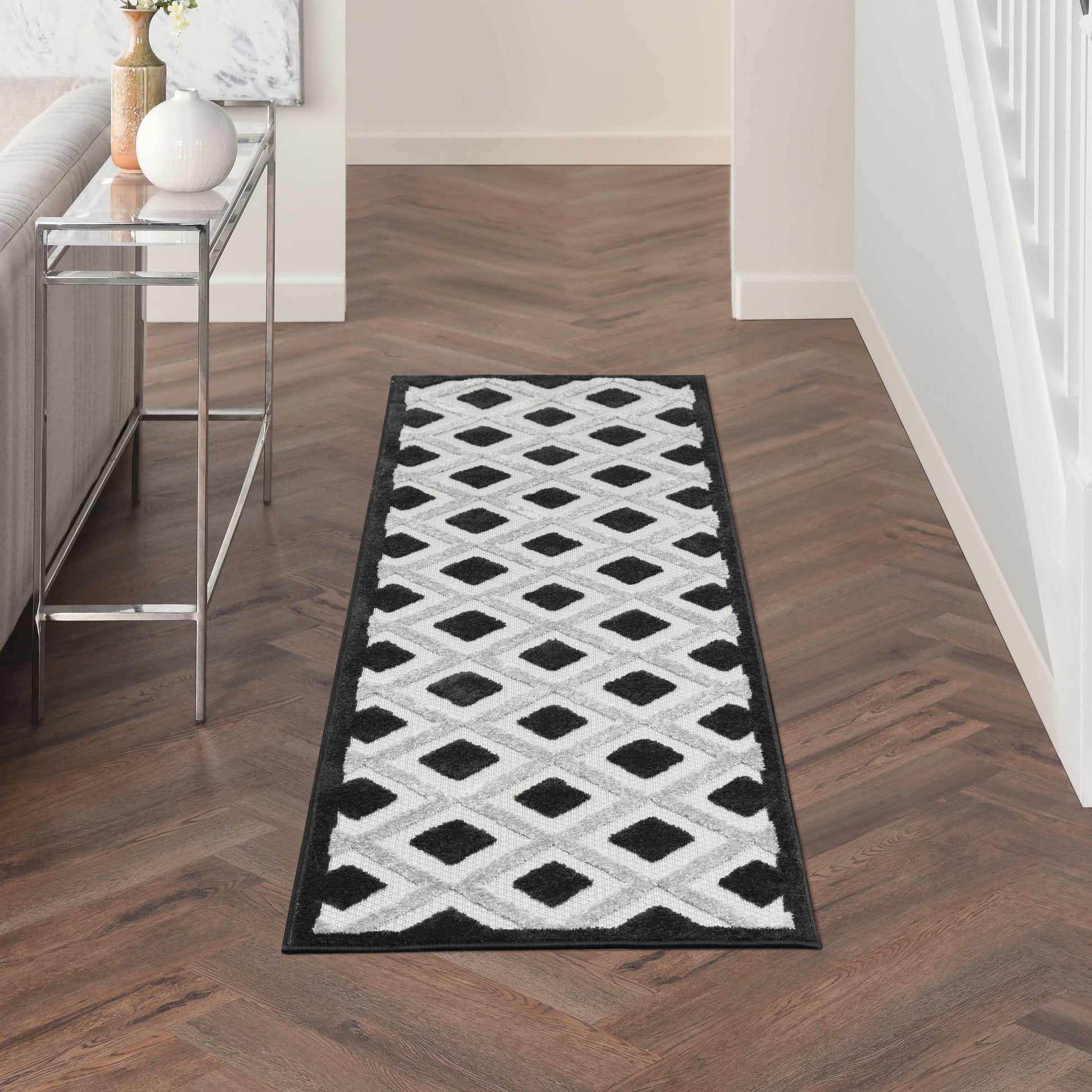 Long hallway runner rug with black border and white diamond lattice pattern, plush pile on dark wood floor