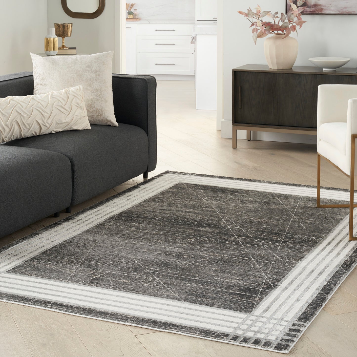 Charcoal gray area rug with light cream border and subtle geometric lines in a modern living room beside a dark sofa.