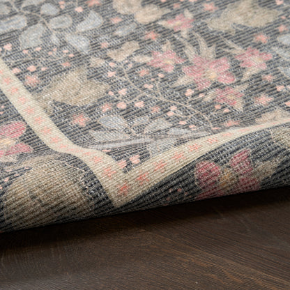 Blue-gray floral woven rug with pink blossoms and ivory border, folded corner on dark wood floor.